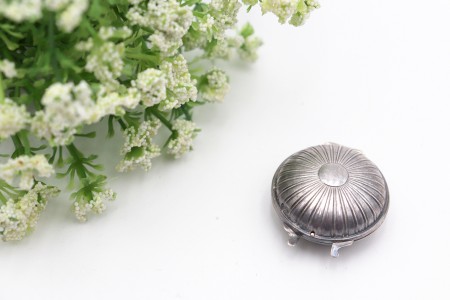 Caixa de comprimidos em prata de forma circular e tampas listadas